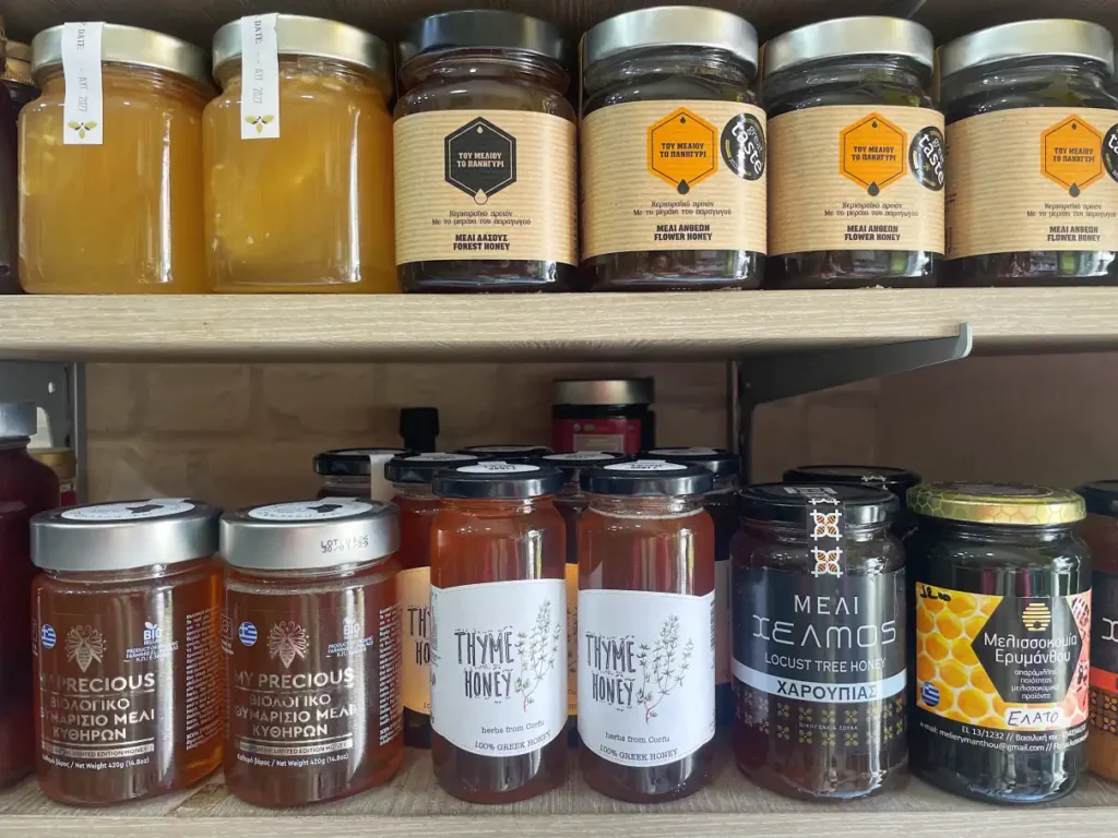 Shelves of Greek honey jars in a Corfu spice shop, including thyme honey, forest honey, flower honey, and locust tree honey